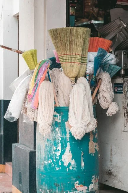 A hand using a feather duster to clean a wooden desk, surrounded by plants and office items.